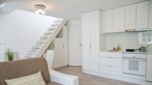 A modern kitchen with white cabinets, a built-in oven, and a dining area with a brown sofa and patterned pillow. - Apartments Hiša Pod Gradom (Ljubljana)