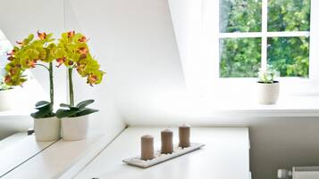 Un baño moderno con un lavamanos blanco, un espejo, una ventana con vistas a la vegetación y dos orquídeas en macetas.