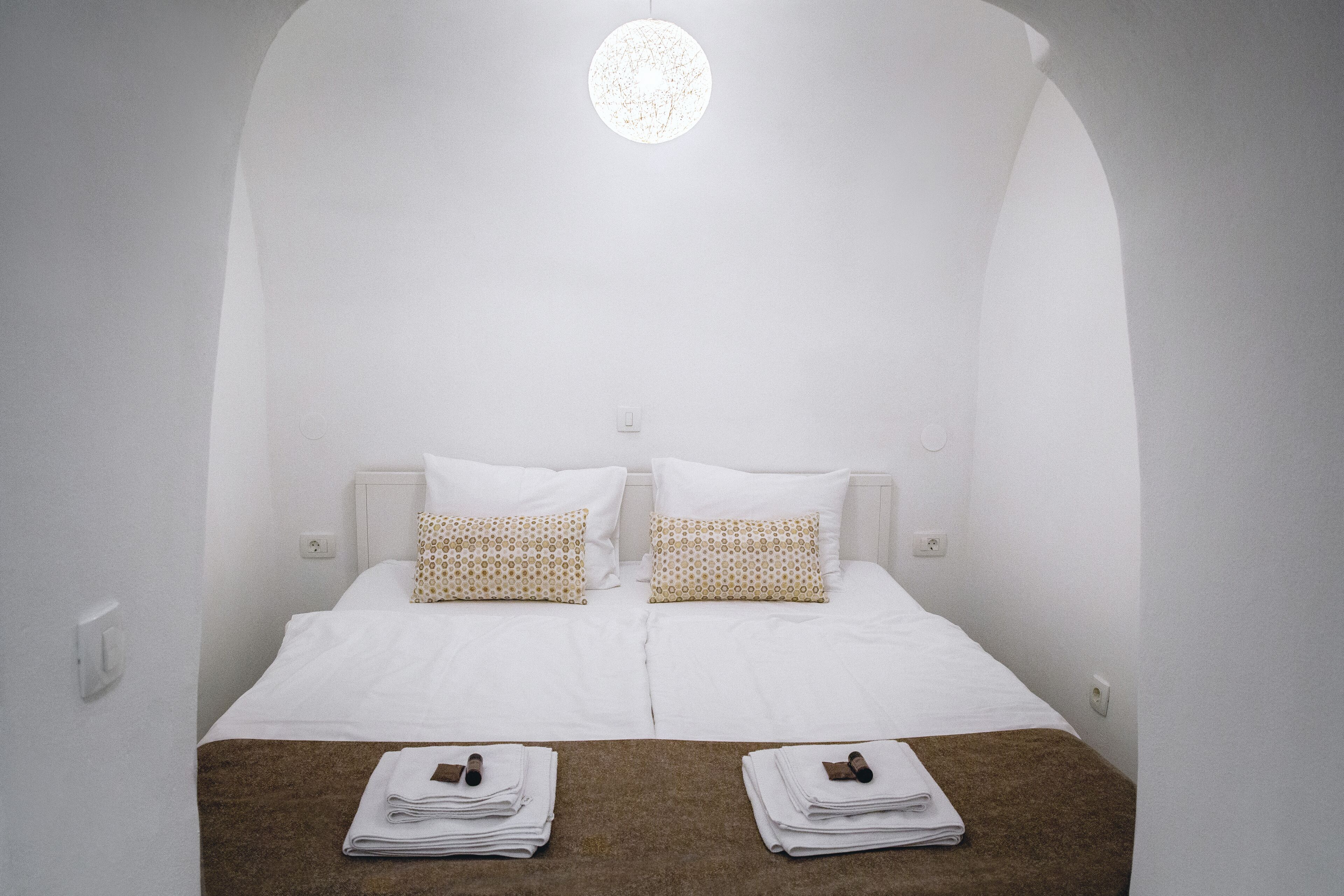 Ein schlichtes Hotelzimmer mit einem großen Bett, zwei Kissen und einer runden Lampe.
