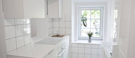 A modern kitchen with white cabinetry, a window with a view of greenery, and a small potted plant on the windowsill.