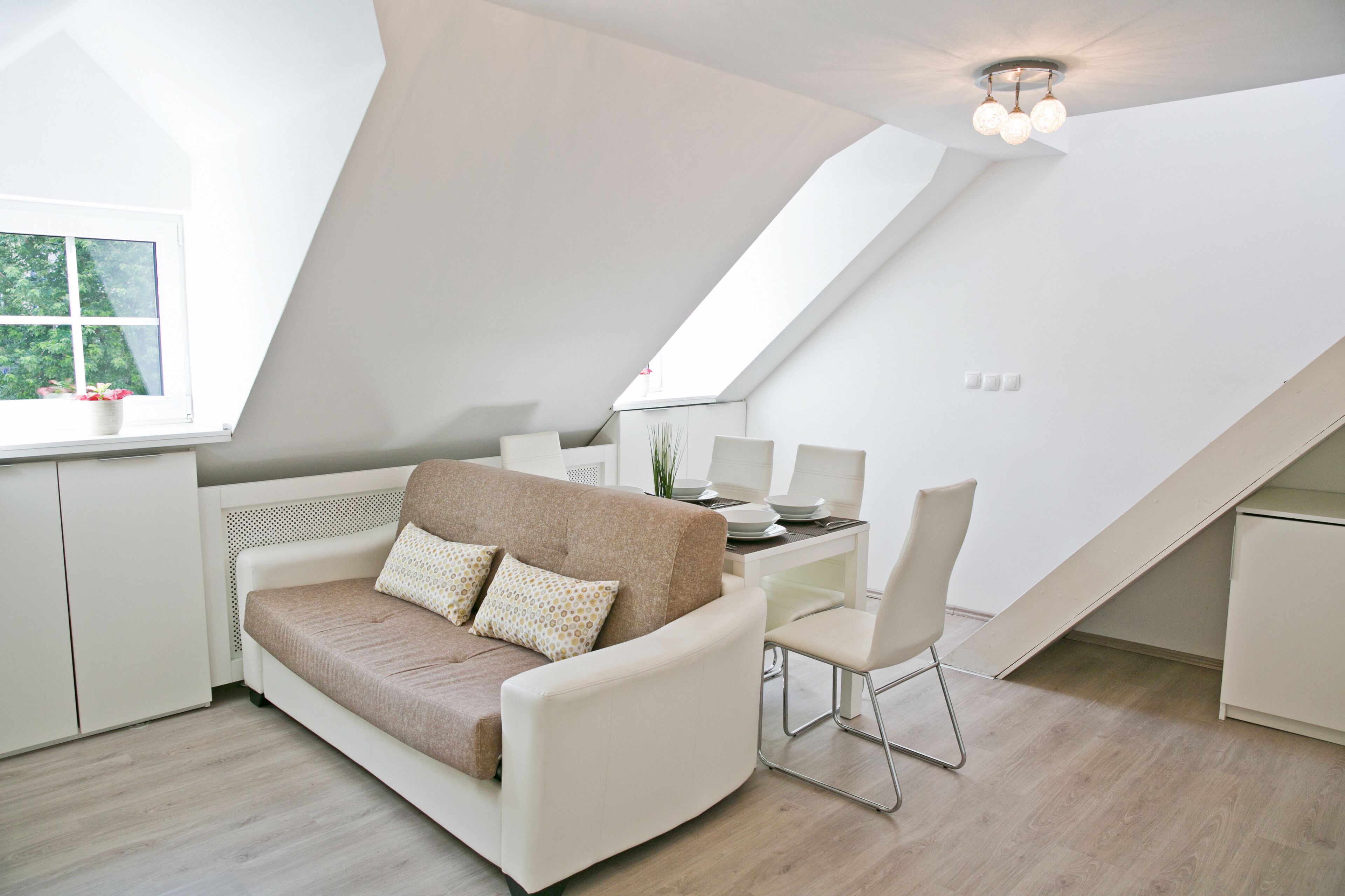 A modern loft bedroom with a sloped ceiling, a white sofa, a dining table, and a chair.