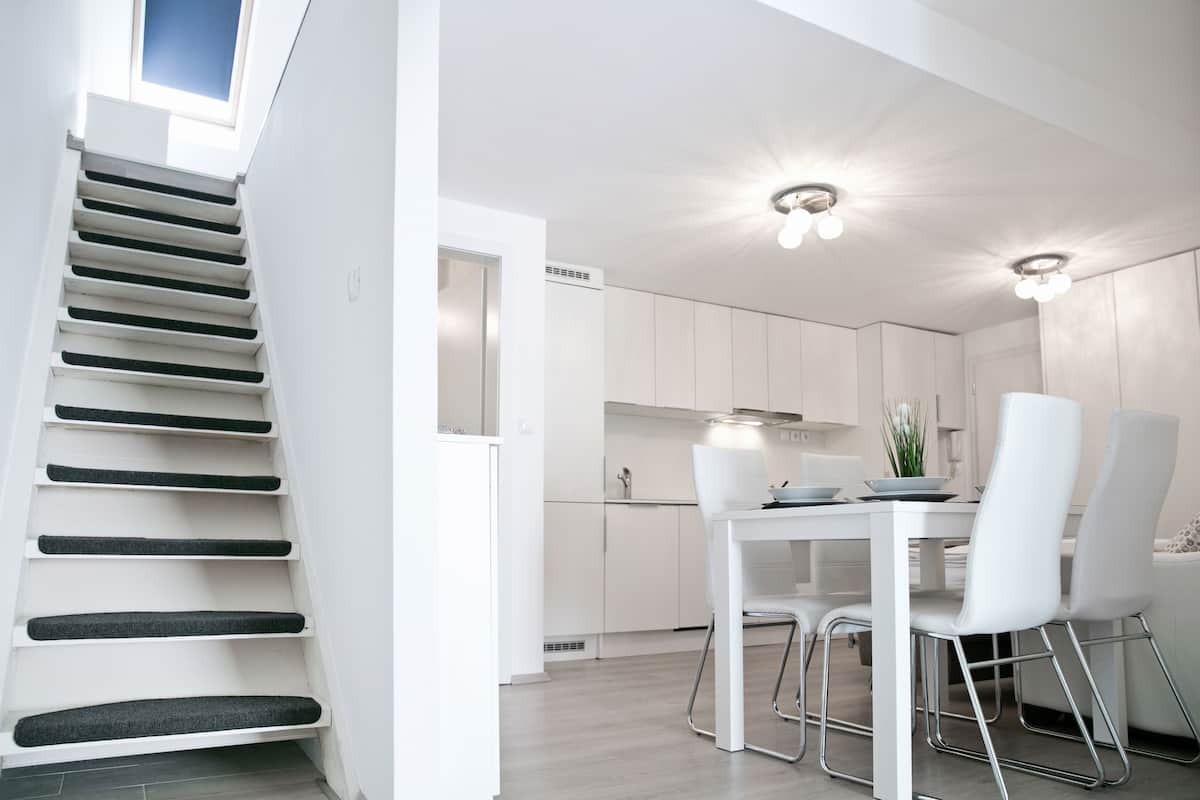 Eine moderne Küche mit weißen Schränken, einem Esstisch mit weißen Stühlen und einer Treppe mit schwarzen Stufen.