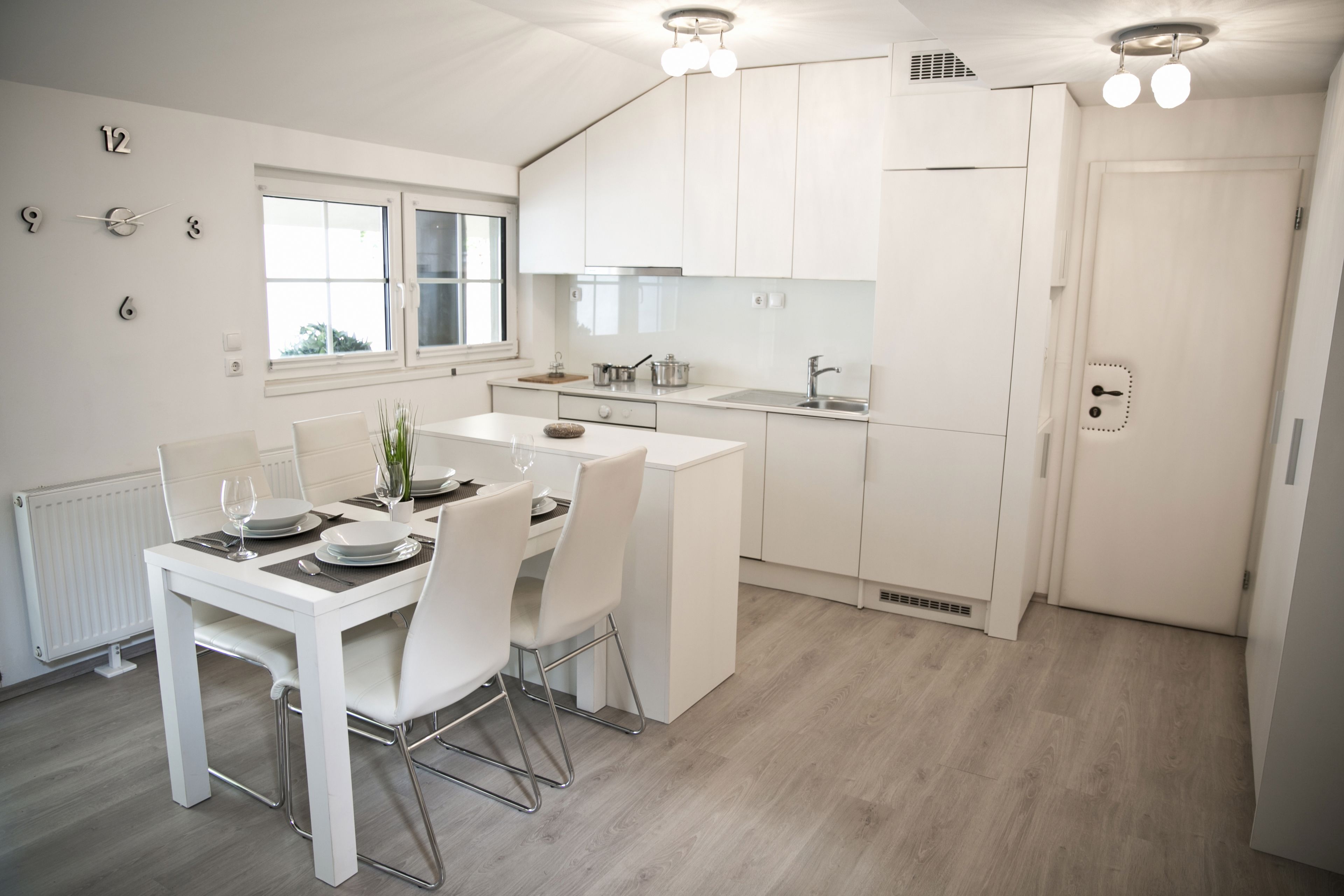 A modern kitchen with white cabinetry, a dining area with a white table and chairs, and a window providing natural light.
