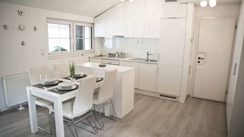 A modern kitchen with white cabinetry, a dining area with a white table and chairs, and a window providing natural light.