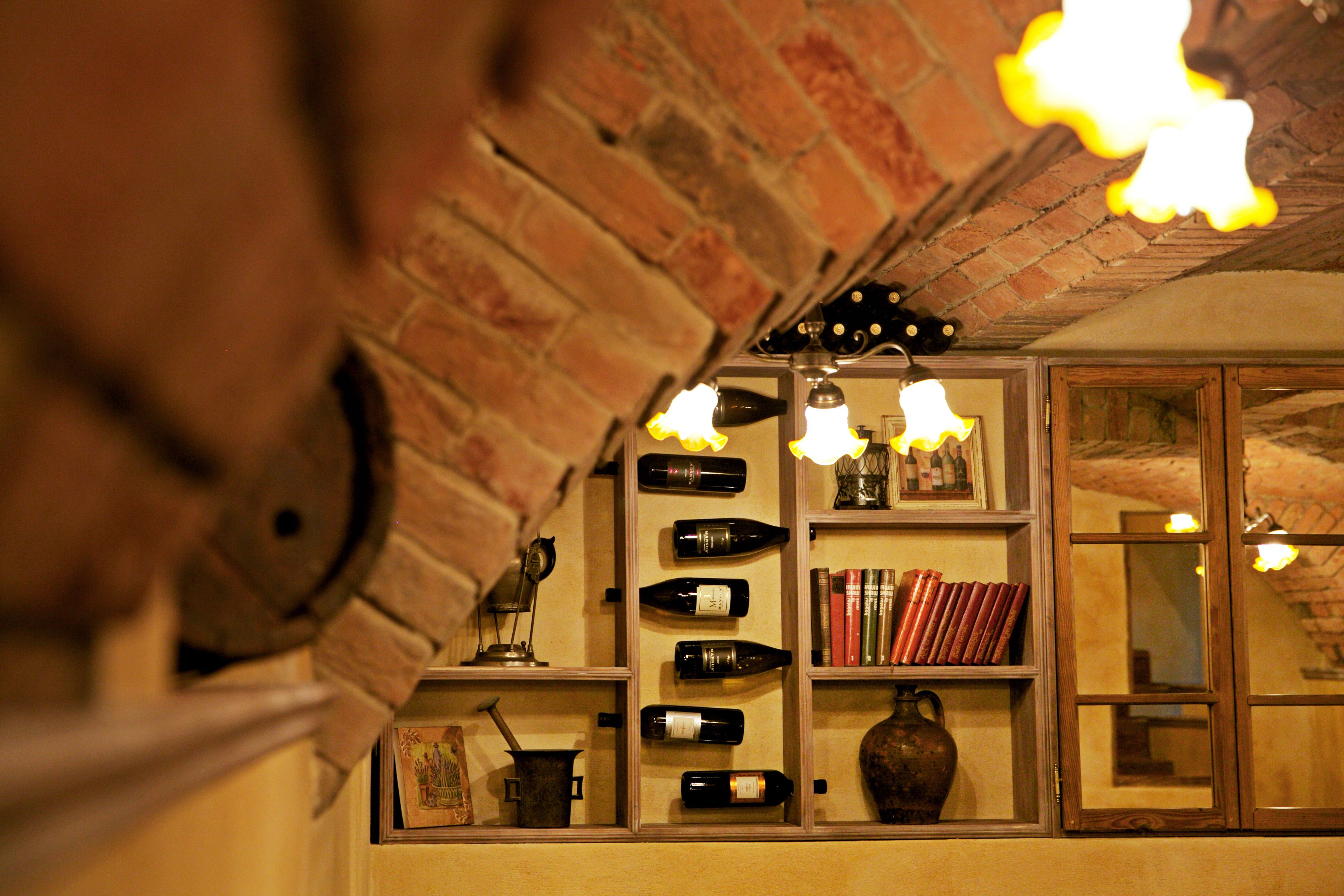 Une pièce avec un mur en briques, des étagères remplies de bouteilles de vin, de livres et un vase.