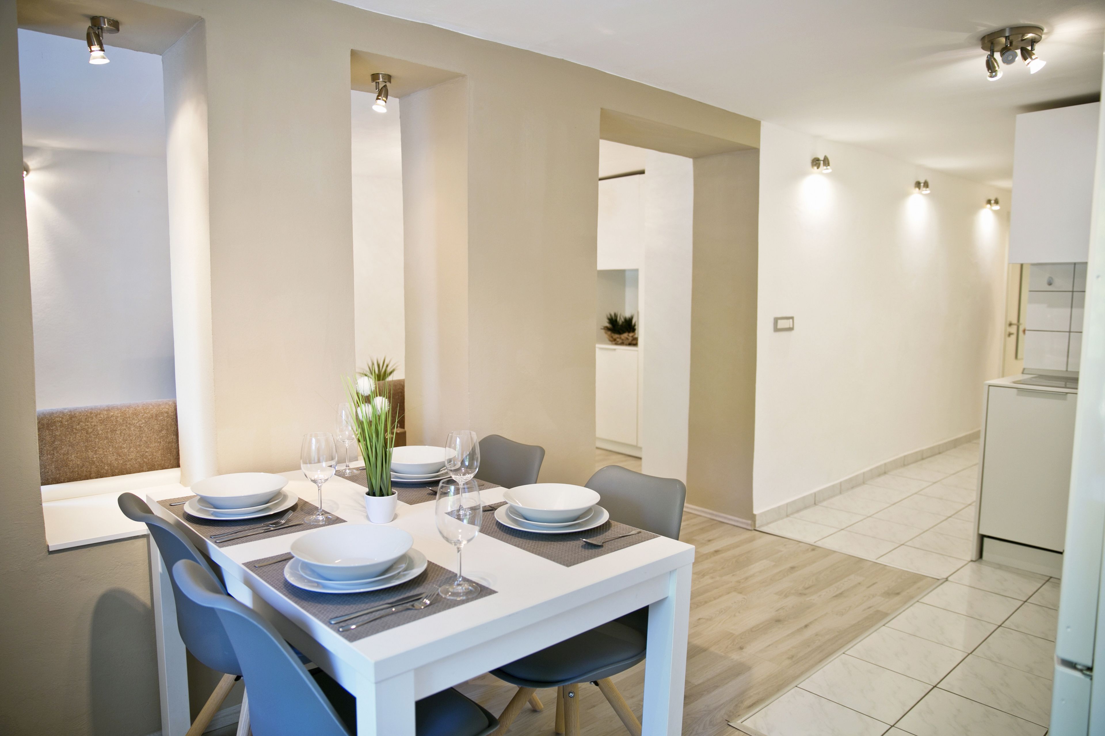A modern dining area with a white table set for four, including plates, glasses, and cutlery.