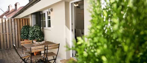 An outdoor patio with a wooden table and chairs, a potted plant, and a view of the house's exterior.