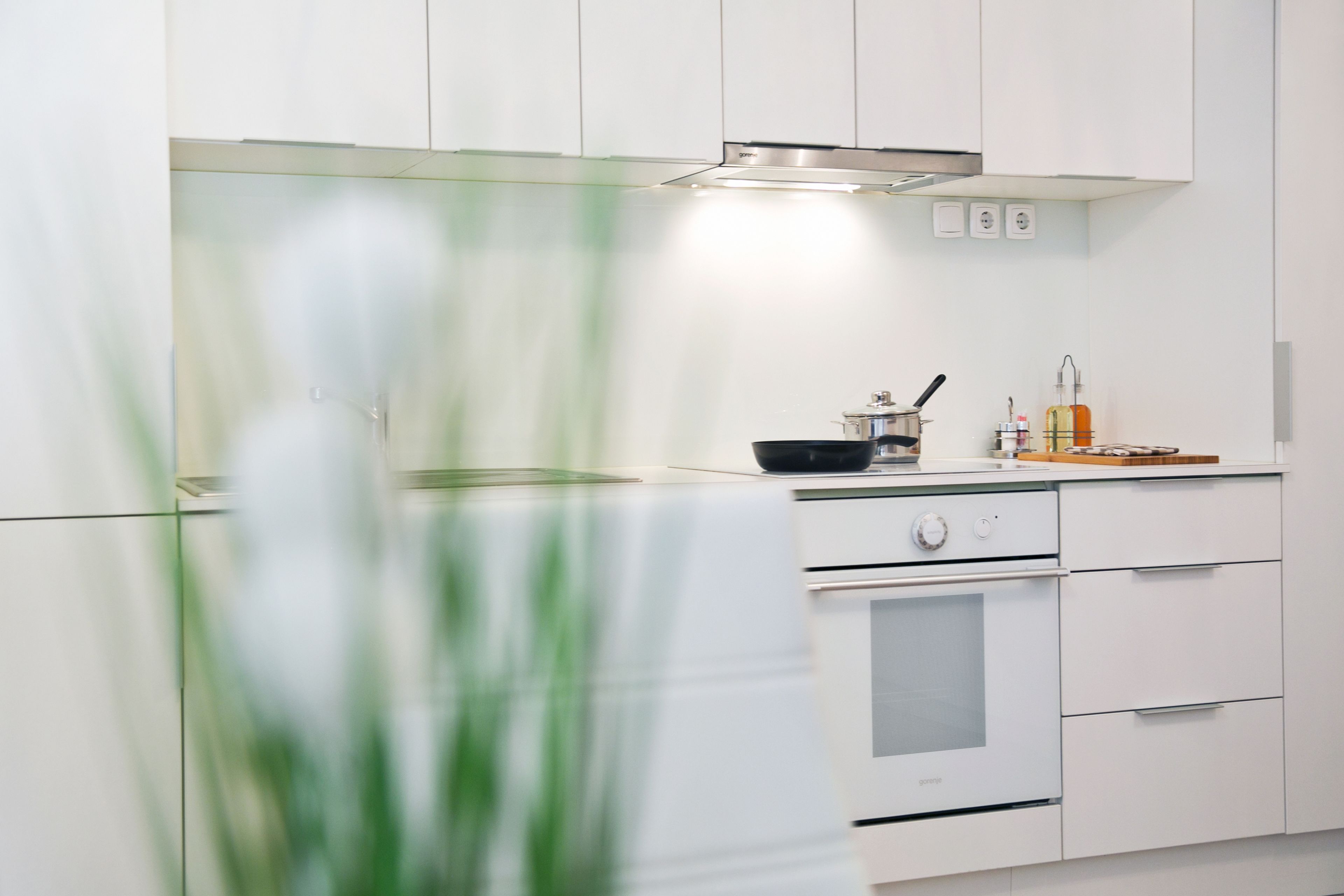 Eine moderne Küche mit weißen Schränken, einem Herd, Backofen und einer Arbeitsplatte mit Topf und Flasche.