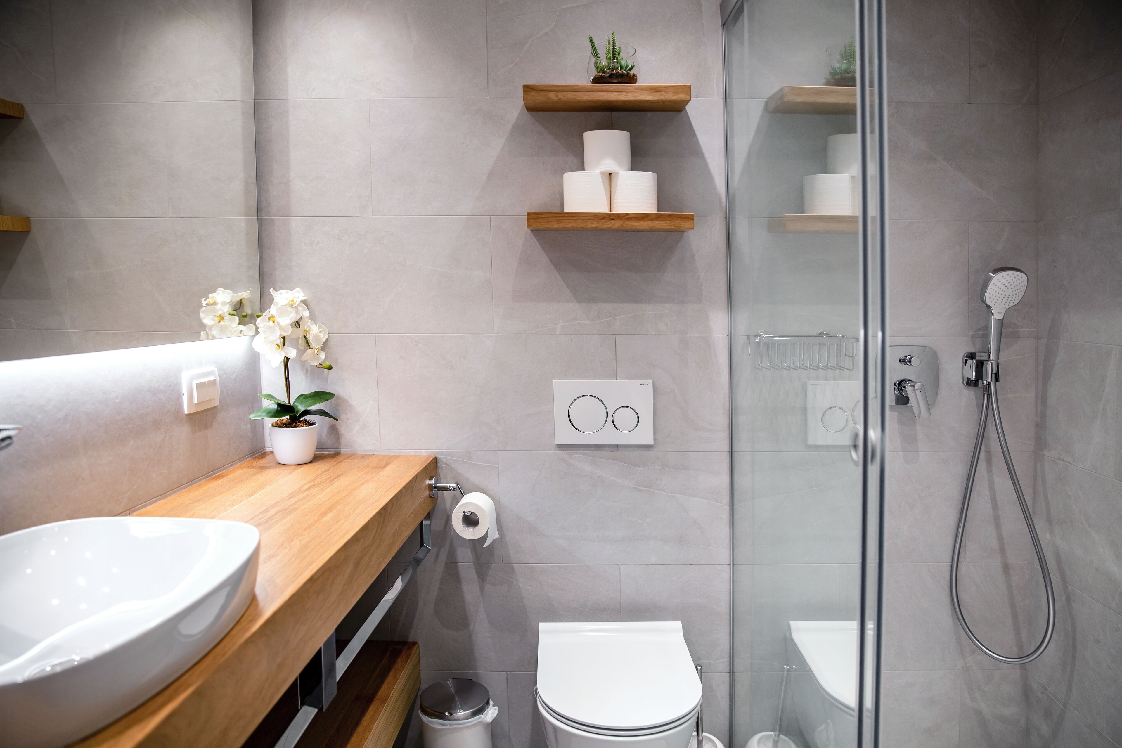 Une salle de bain moderne avec un meuble-lavabo en bois, un lavabo blanc, une cabine de douche en verre et des toilettes.