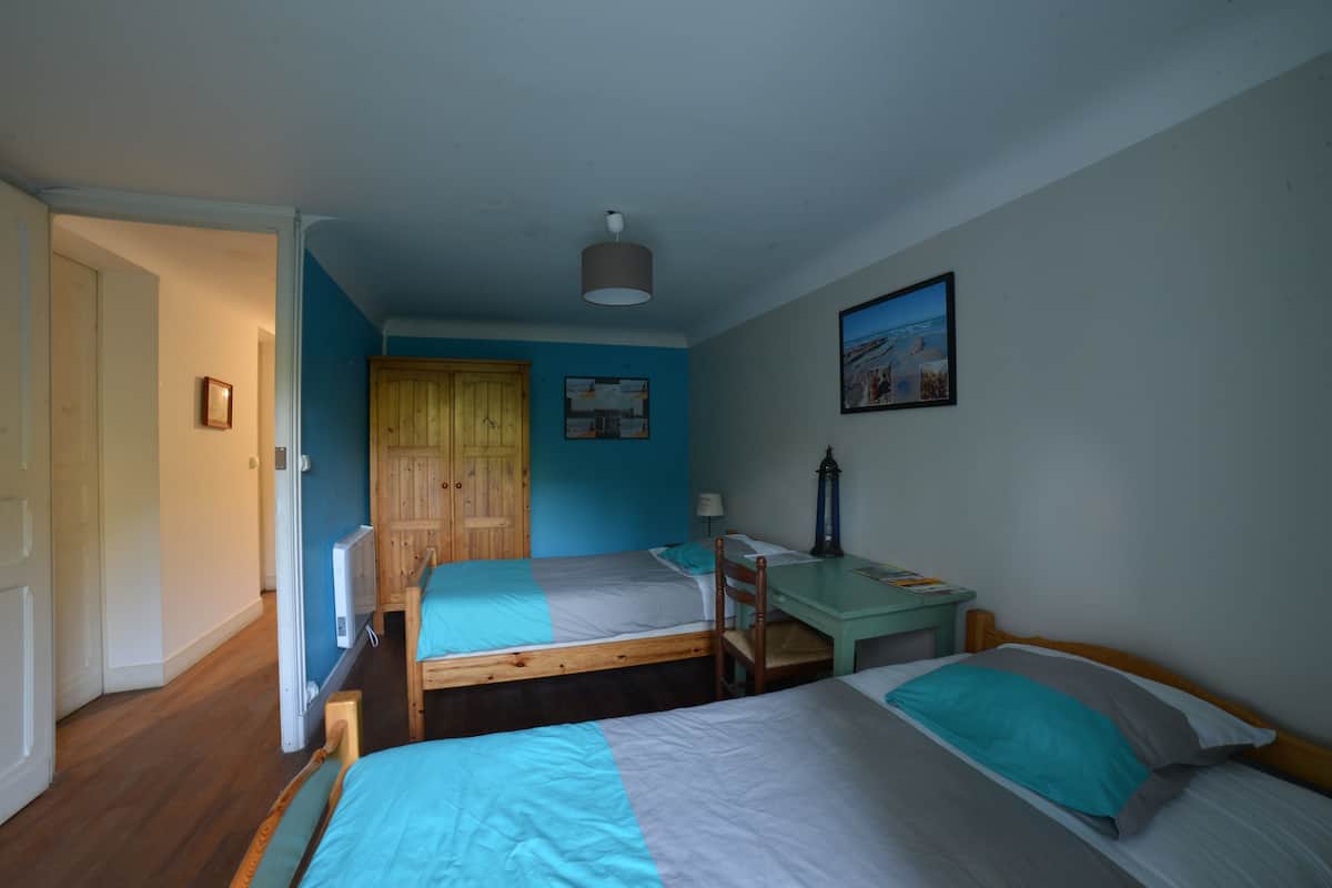 A bedroom with two single beds, a wooden wardrobe, a desk, and a picture on the wall.