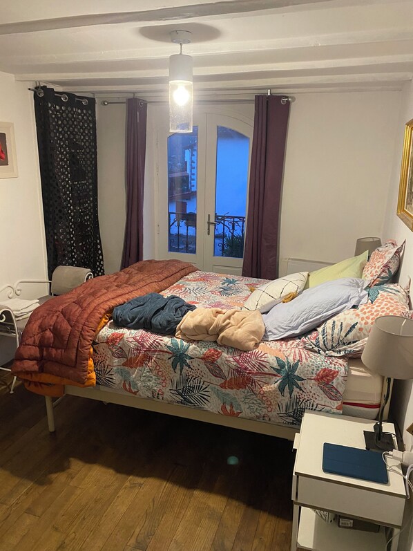 A bedroom with a bed, a bedside table, a lamp, a window with curtains, and a view of the outside balcony. - Etxe Arrosa (Saint-Martin-d'Arrossa)