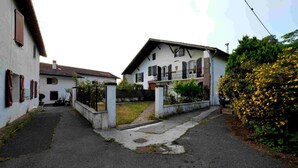 A narrow street with two white buildings, one with a balcony and a small garden. - Etxe Arrosa (Saint-Martin-d'Arrossa)