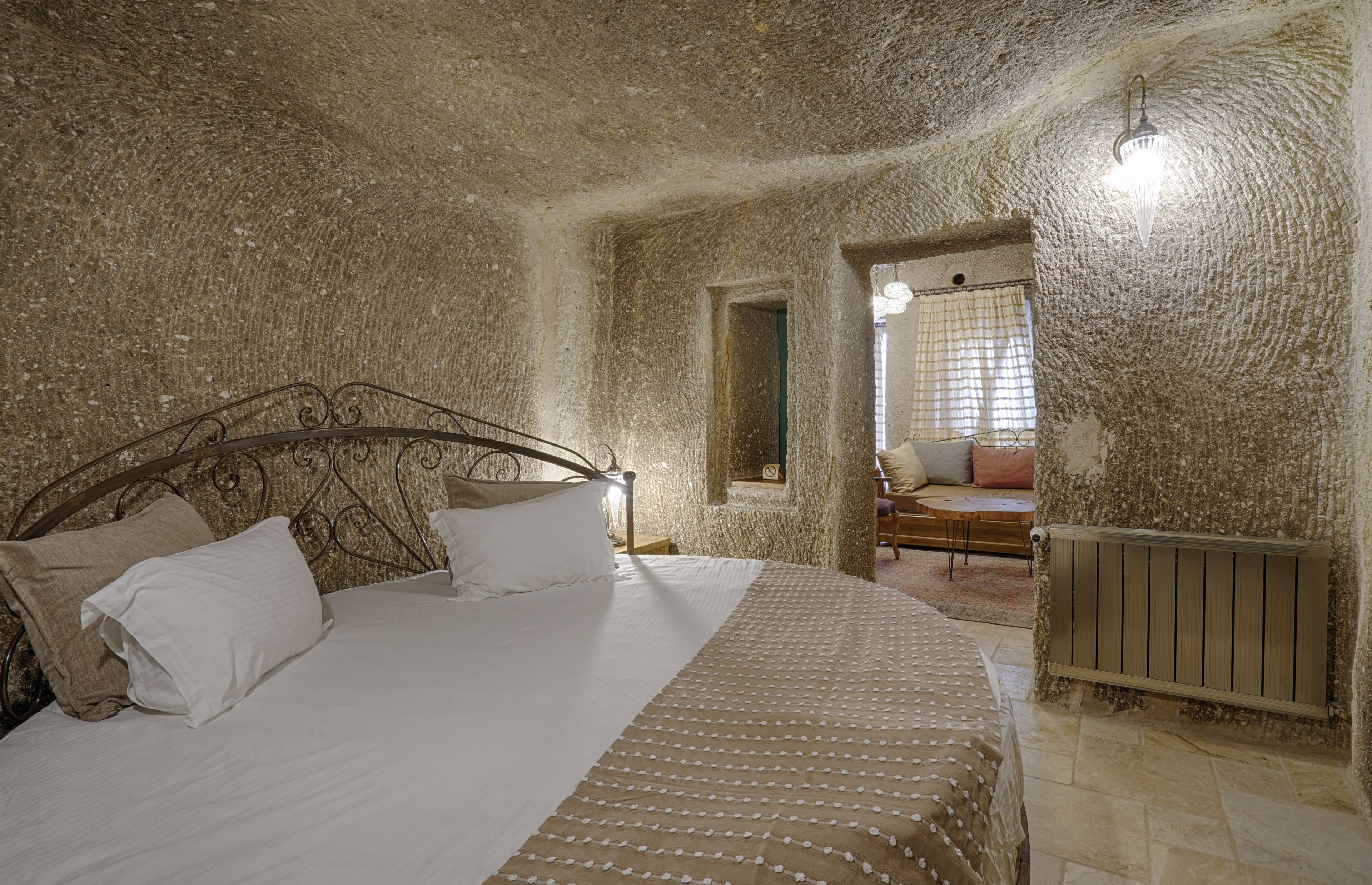 A bedroom with a stone wall, a bed with white and patterned bedding, a wooden headboard, and a radiator.