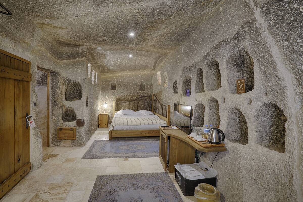 A room with a stone wall, a wooden bed, a television, and a small wooden cabinet.