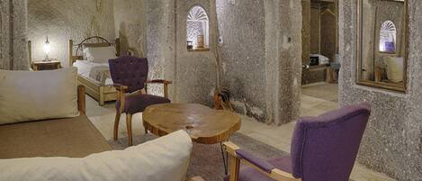 A room with a bed, two purple chairs, a wooden table, and a mirror.
