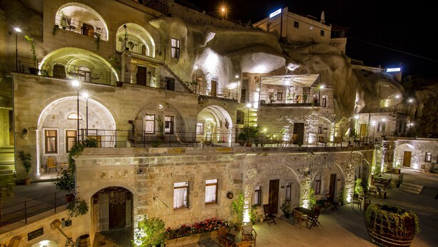 Un edificio storico con numerosi balconi, archi in pietra e zone con posti a sedere all'aperto, adornate da piante in vaso.
