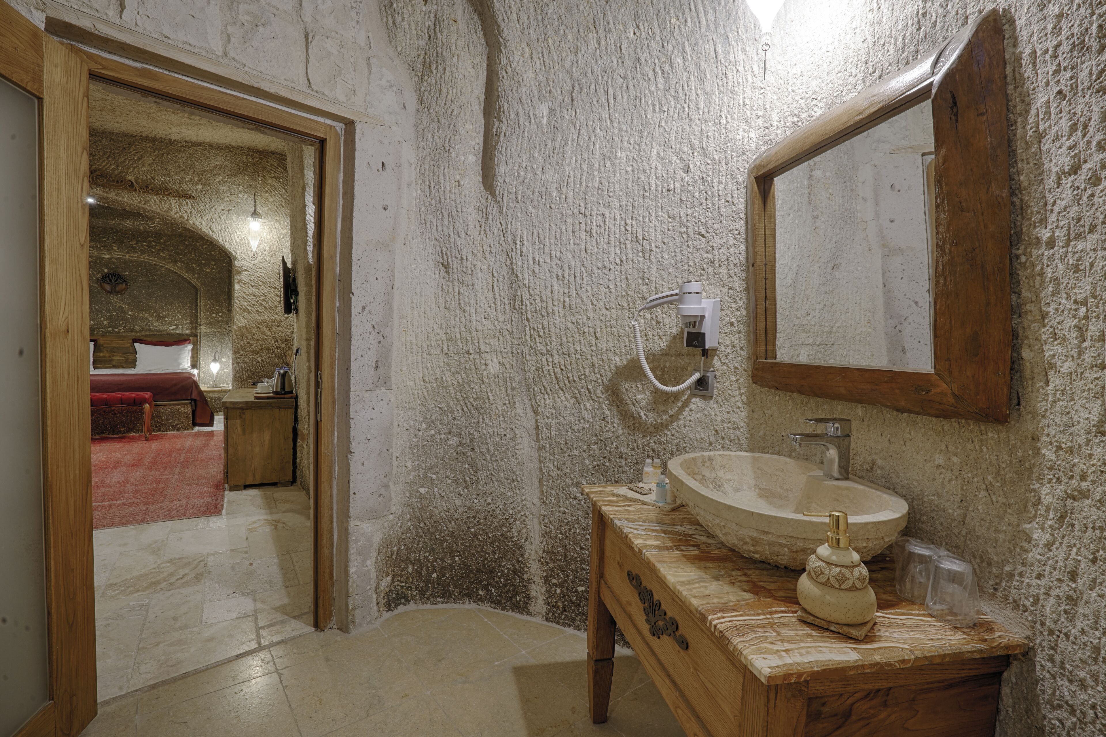 Un baño con pared de piedra, tocador de madera, espejo grande y lavamanos.