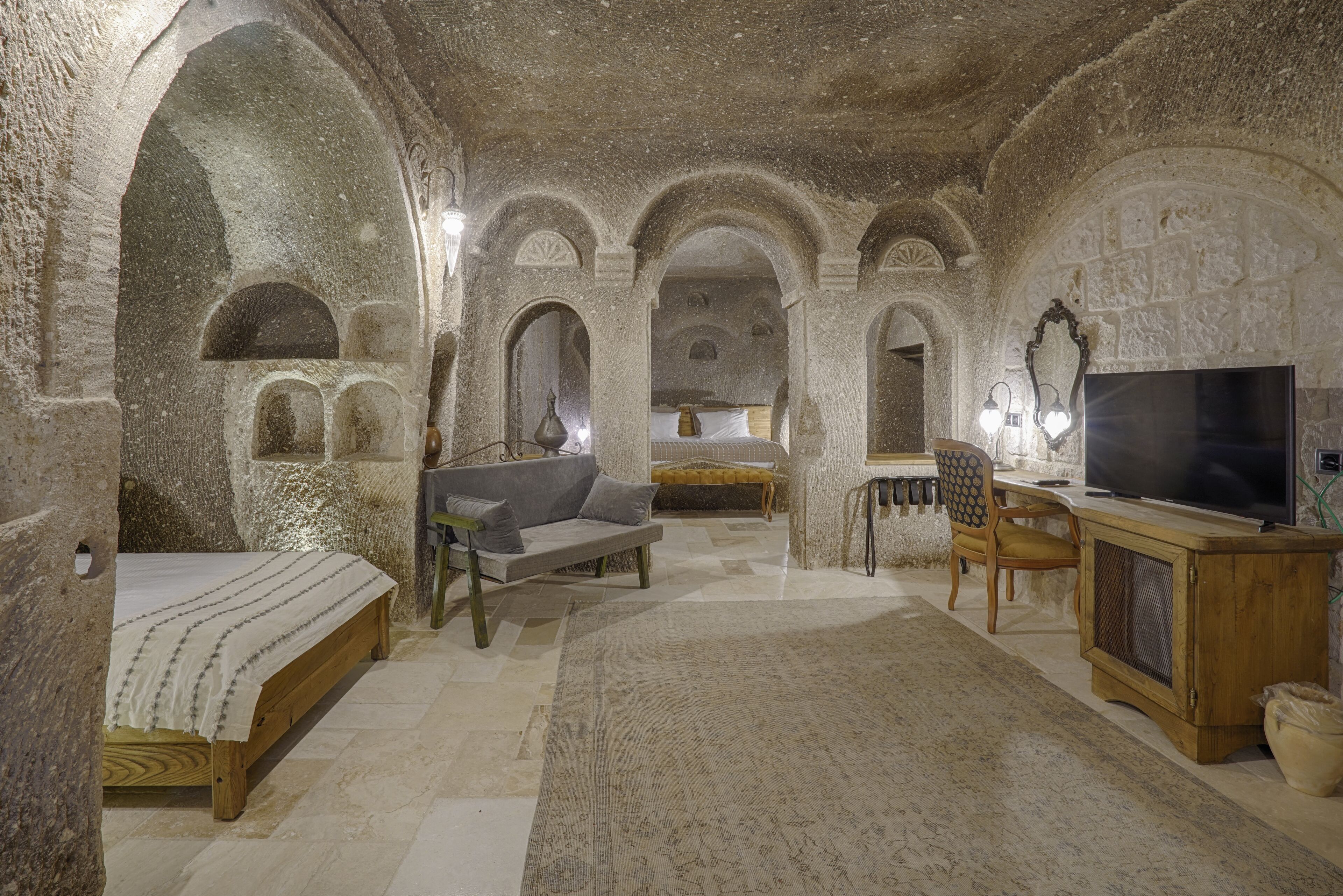 A stone-walled room with a bed, a sofa, a TV, and a desk.