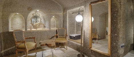A room with a stone wall, a large mirror, and two wooden chairs.