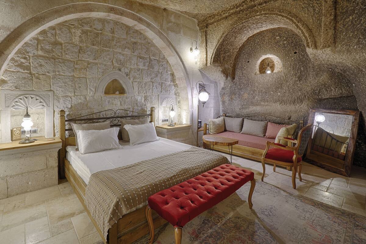 A stone-walled room with a bed, bench, and seating area.