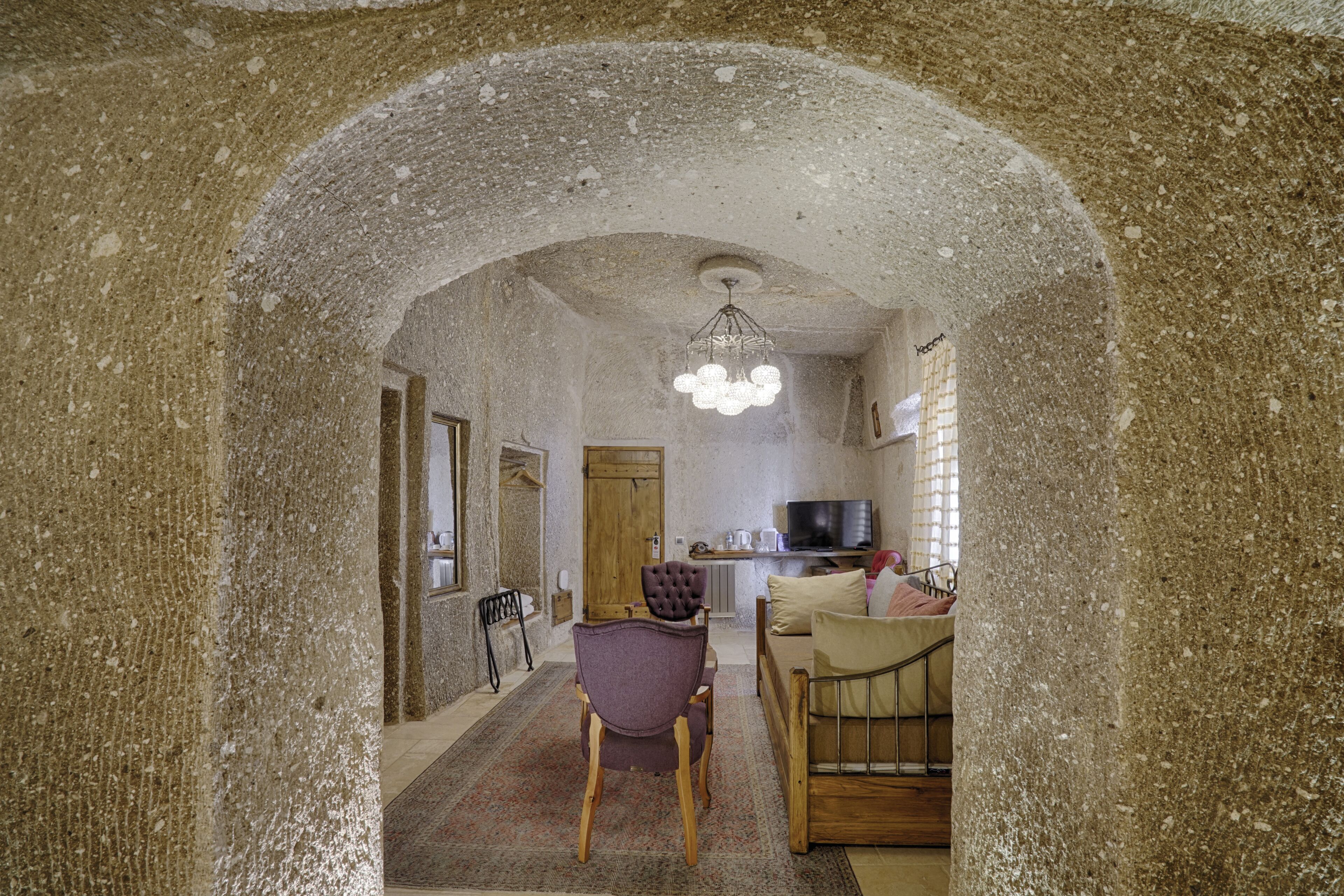 Un intérieur rustique, agrémenté d’une arche en pierre qui mène à un espace de vie comprenant un canapé, un téléviseur et une table à manger en bois.