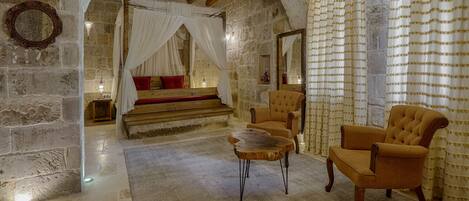 A stone-walled room with a four-poster bed, a wooden bench, and two armchairs.