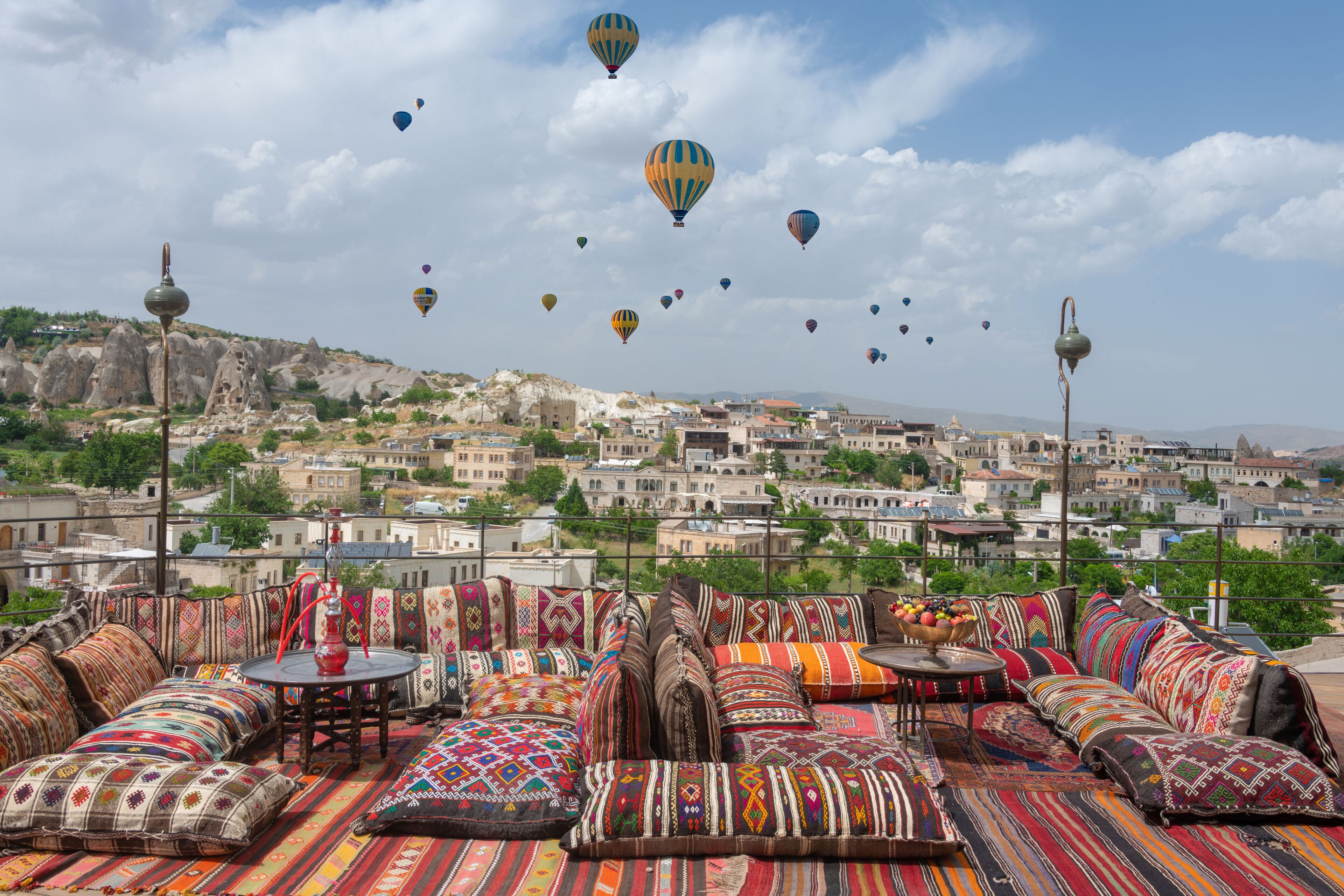 Un espacio de estar en la azotea con cojines de colores y vistas a un paisaje urbano con globos aerostáticos.
