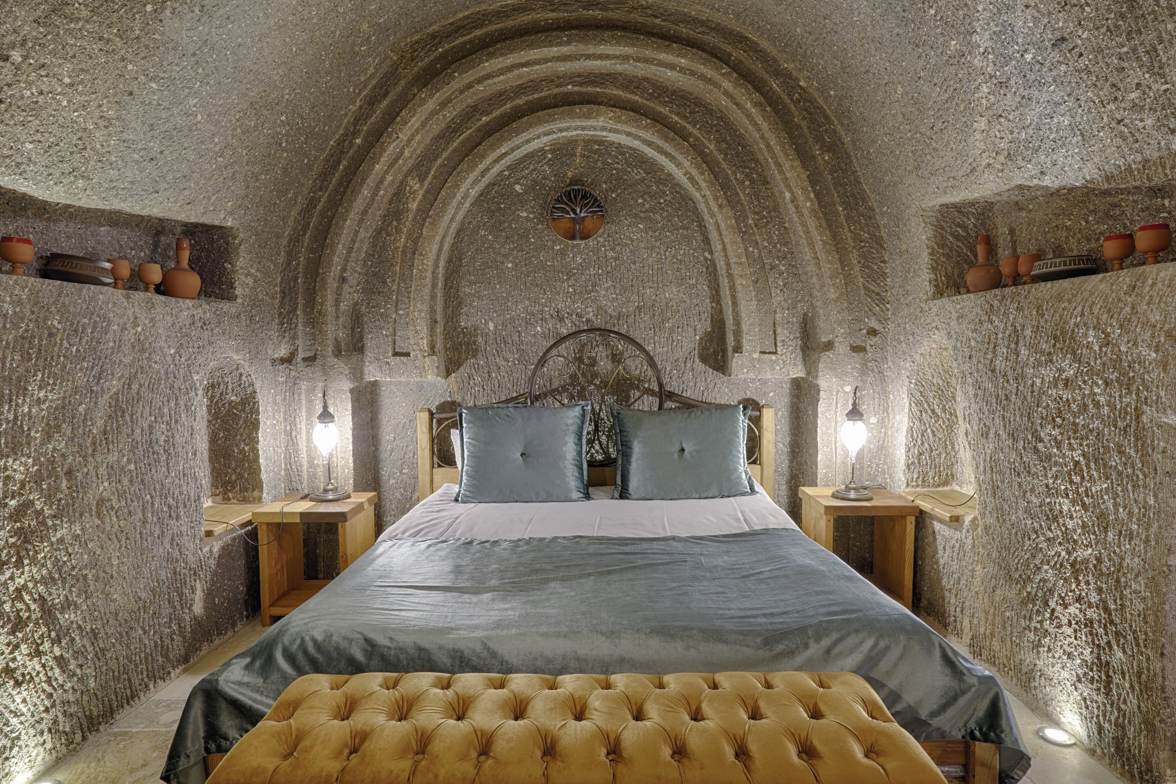 A rustic stone-walled bedroom with a bed, two nightstands, and a bench.