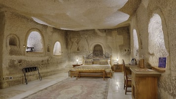 A room with a bed, a desk, and a chair. There are arched windows and a rug on the floor.