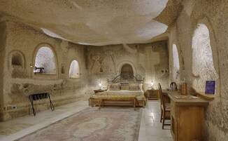 A room with a bed, a desk, and a chair. There are arched windows and a rug on the floor.