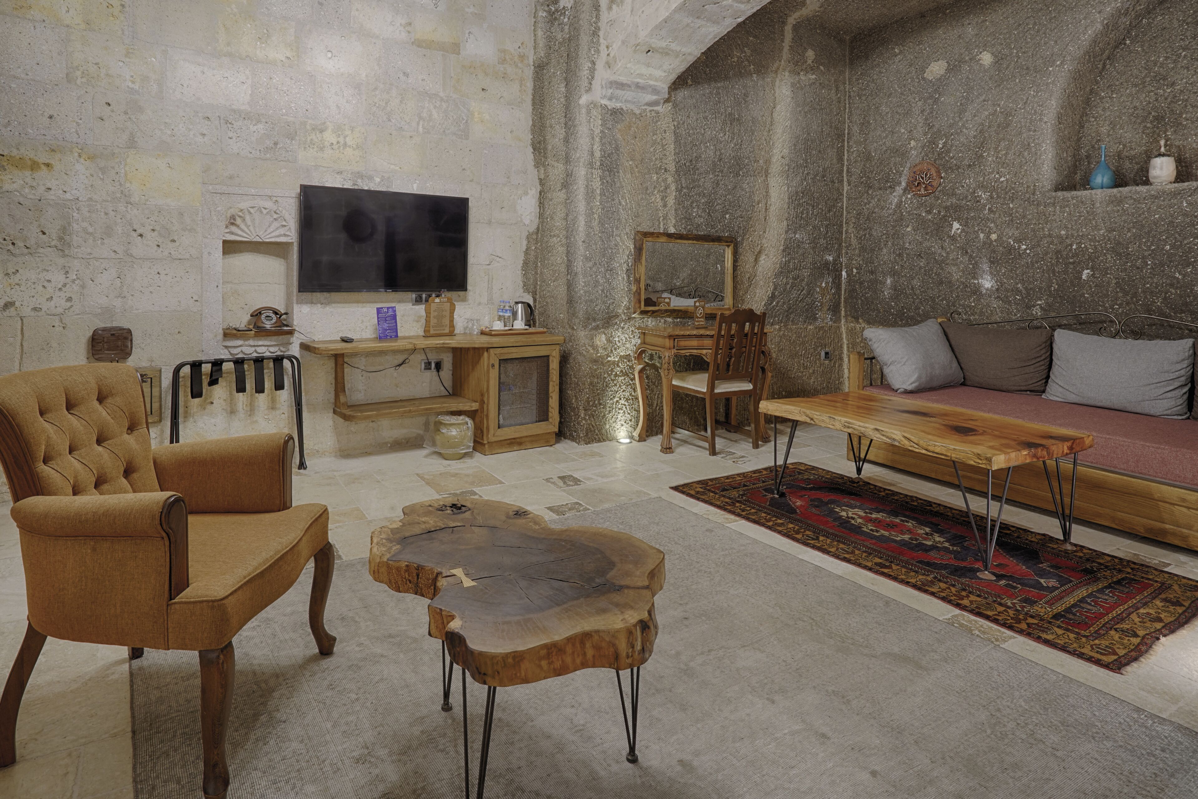 A rustic living room with a stone wall, a wooden coffee table, a sofa, and a television.