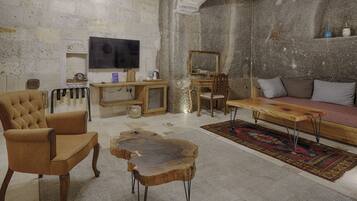 A rustic living room with a stone wall, a wooden coffee table, a sofa, and a television.