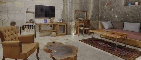 A rustic living room with a stone wall, a wooden coffee table, a sofa, and a television.