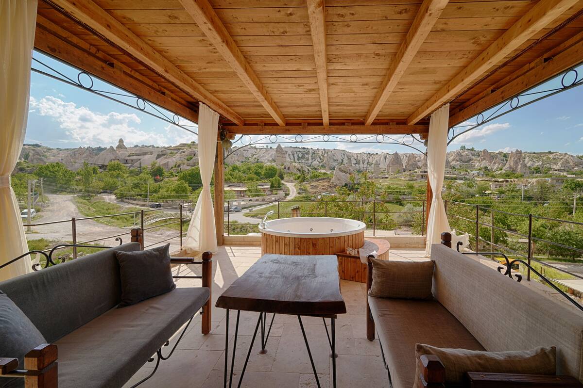 A wooden pergola with a hot tub, sofas, and a view of a mountainous landscape.