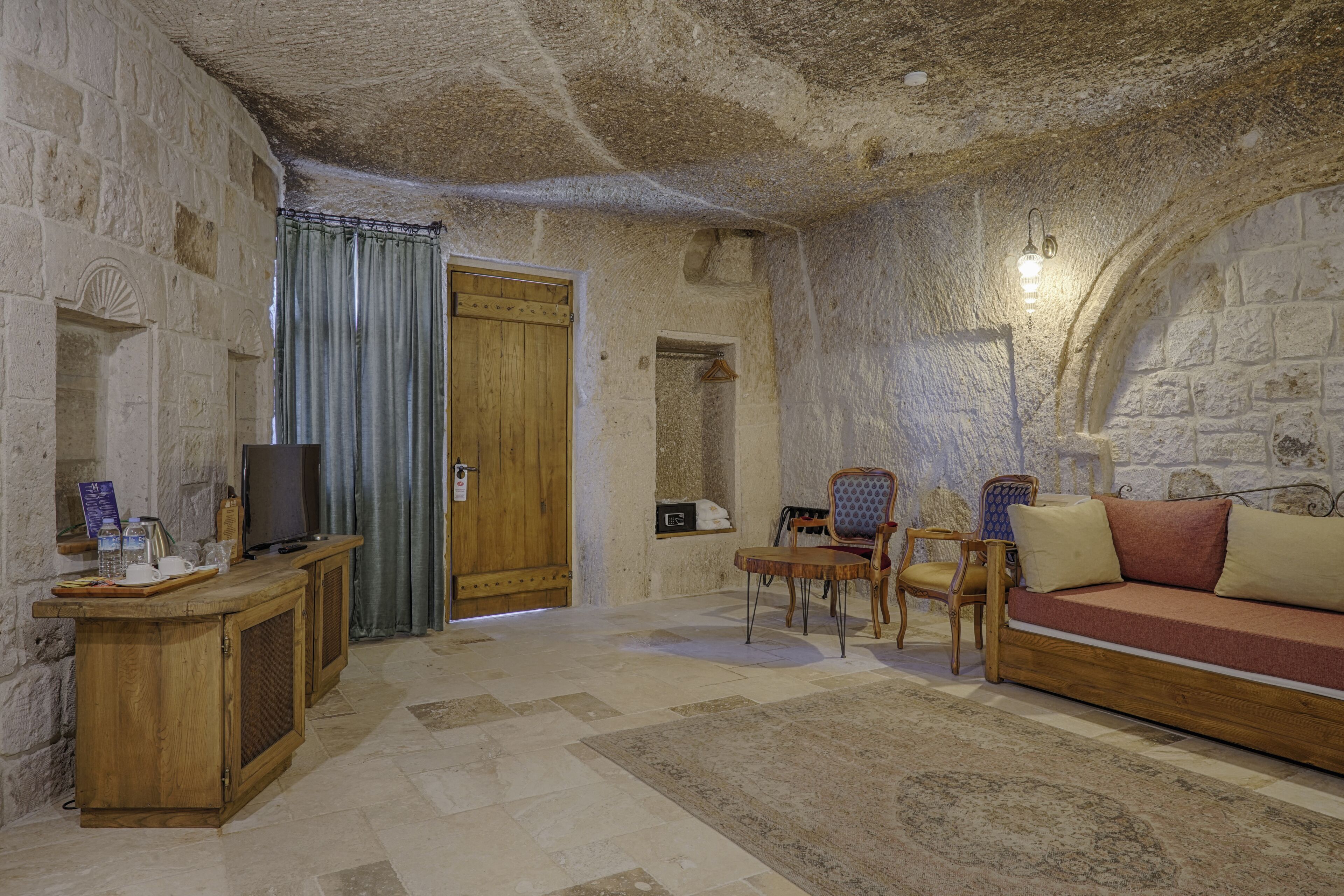 A stone-walled room with a wooden sofa, a television on a wooden cabinet, and a small table with chairs.