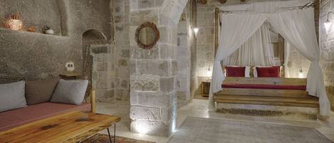 Una habitación rústica con paredes de piedra, un banco de madera, una cama con almohadones rojos y un dosel.