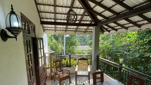 A covered outdoor area with a wooden table and chairs, a railing, and a view of greenery. - New Magnet Villa (Hikkaduwa)