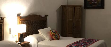 A hotel room with two beds, a wooden headboard, a nightstand with a lamp, a wardrobe, and a framed painting on the wall.