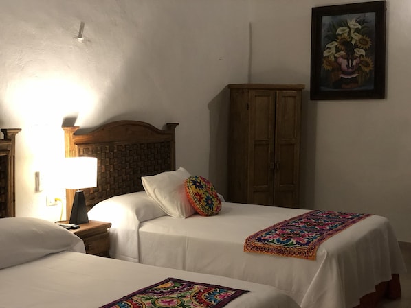 Habitación de hotel con dos camas, cabecera de madera, mesita de noche con lámpara, armario y un cuadro enmarcado en la pared.