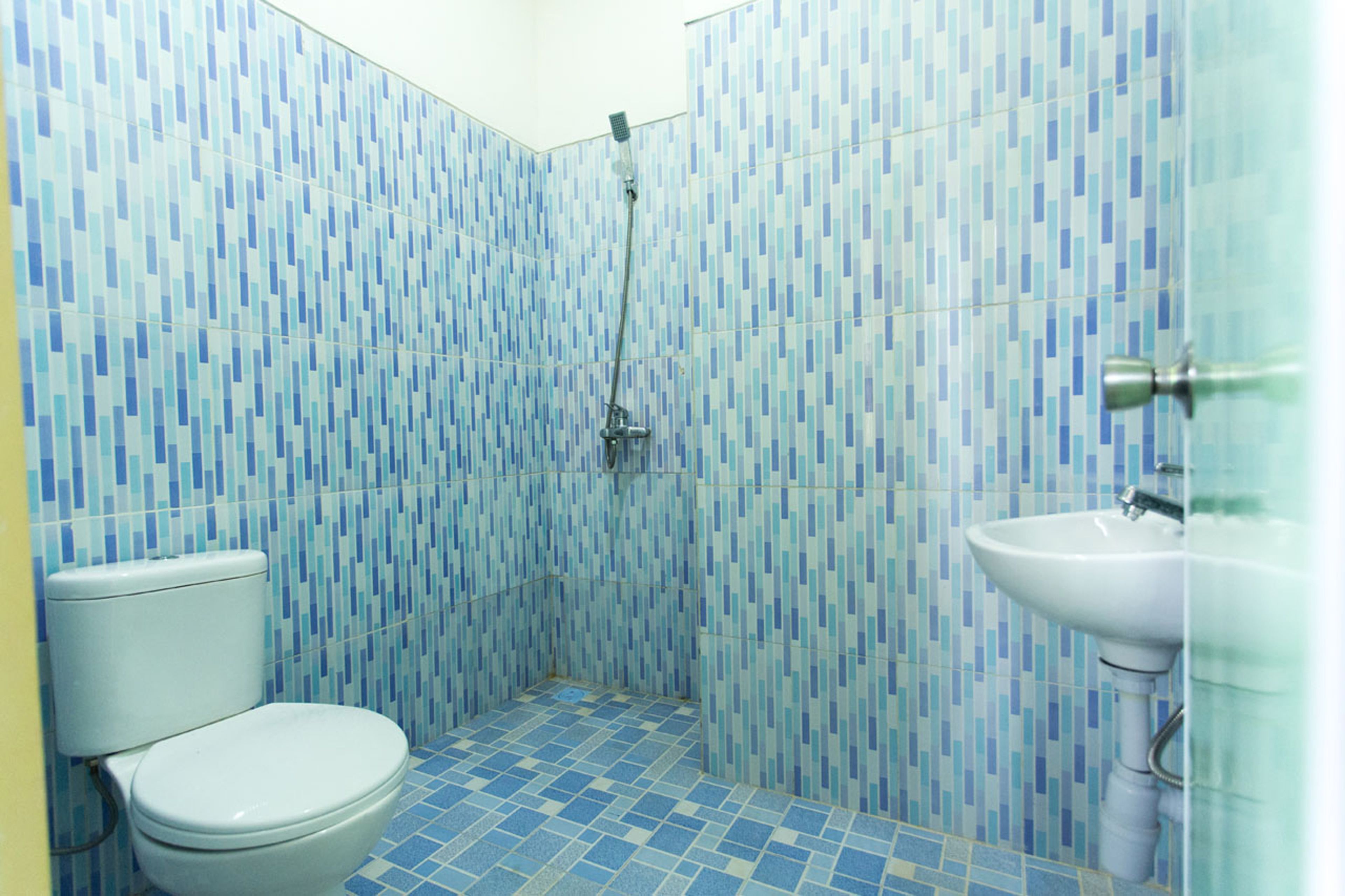 A bathroom with a tiled floor and walls, a toilet, a shower, and a sink.