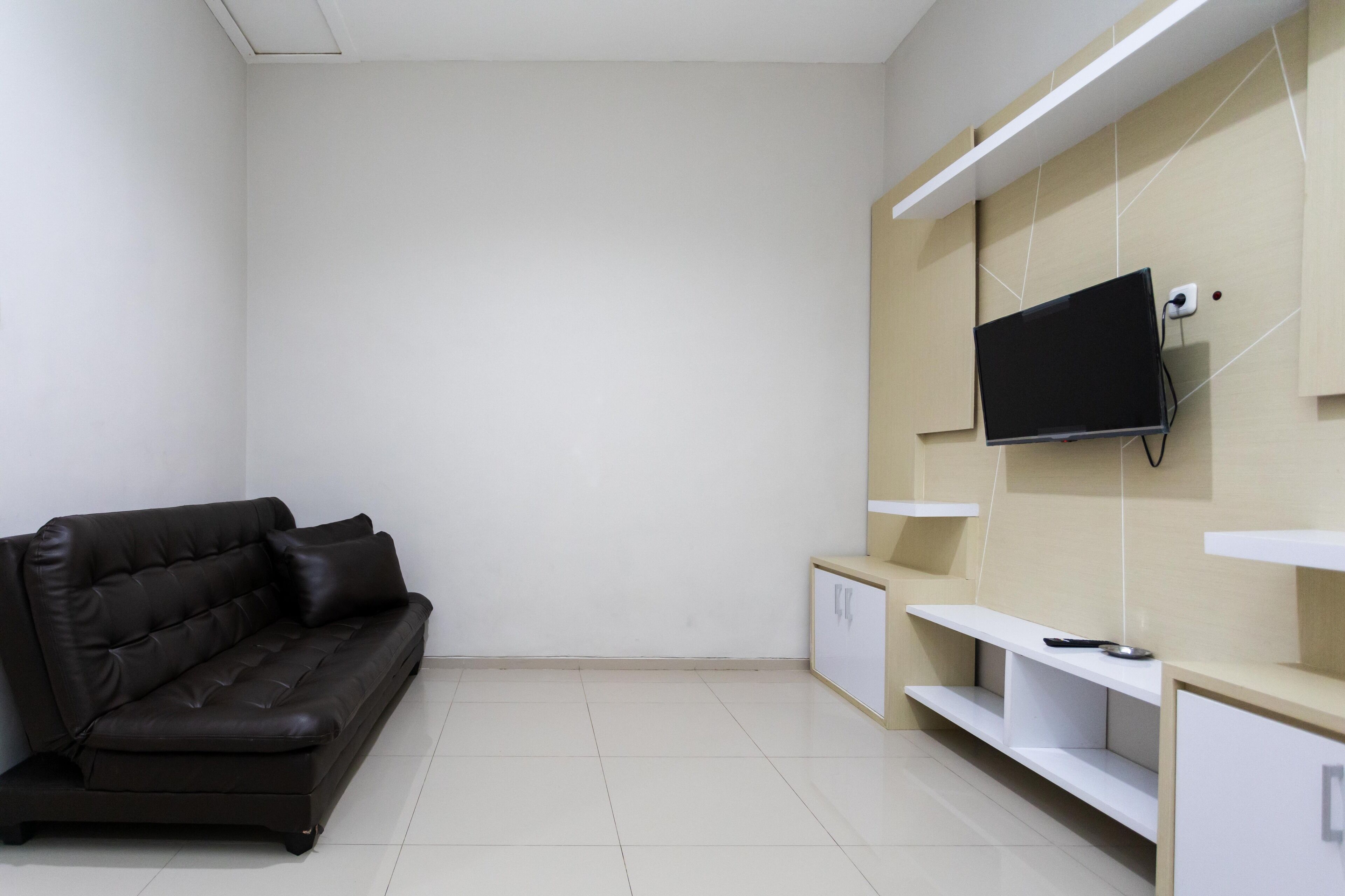 A modern room with a black leather sofa, a flat-screen TV mounted on the wall, and built-in shelving.