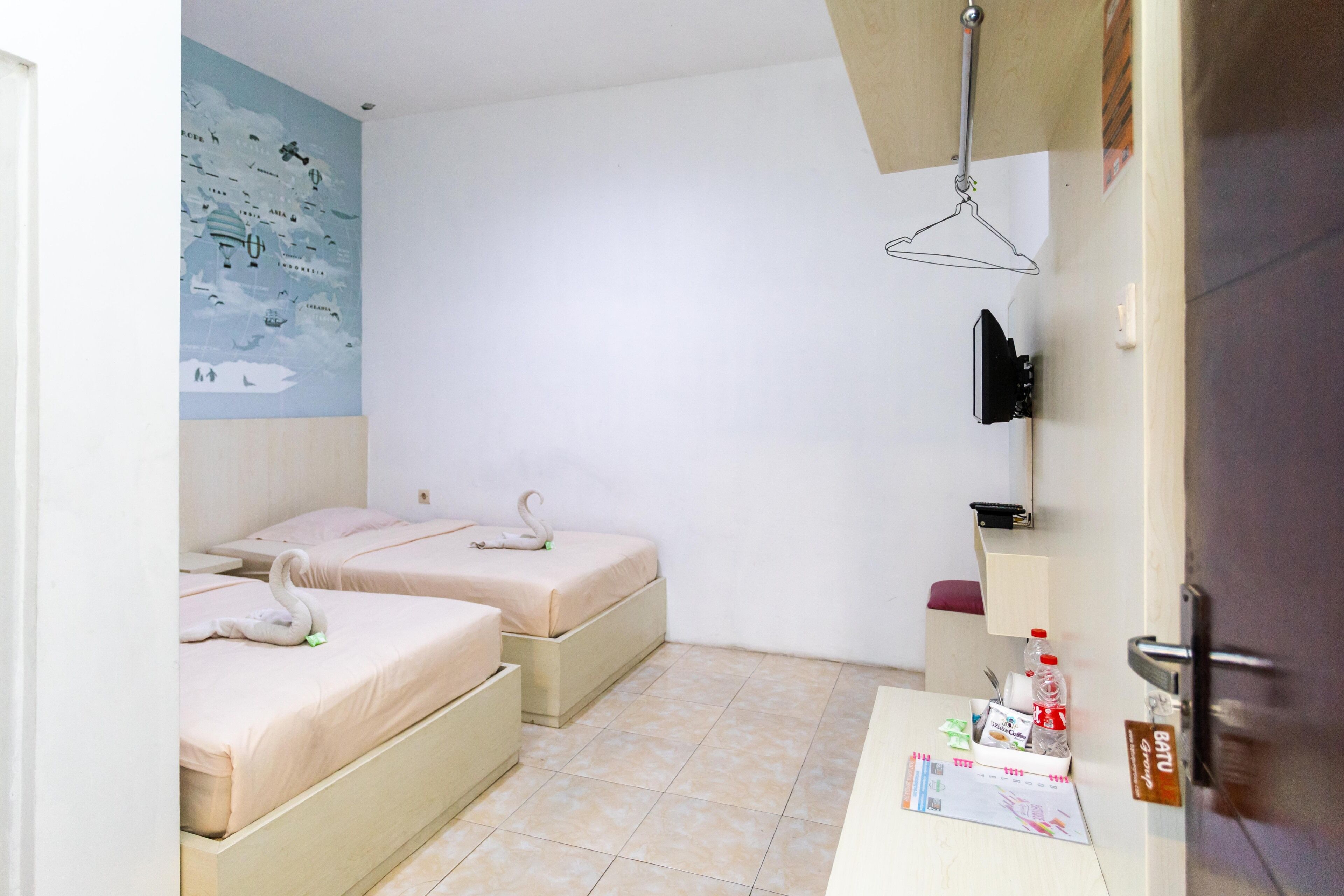 Habitación de hotel con dos camas, un escritorio pequeño con artículos de aseo, un mapa en la pared y una lámpara colgante.