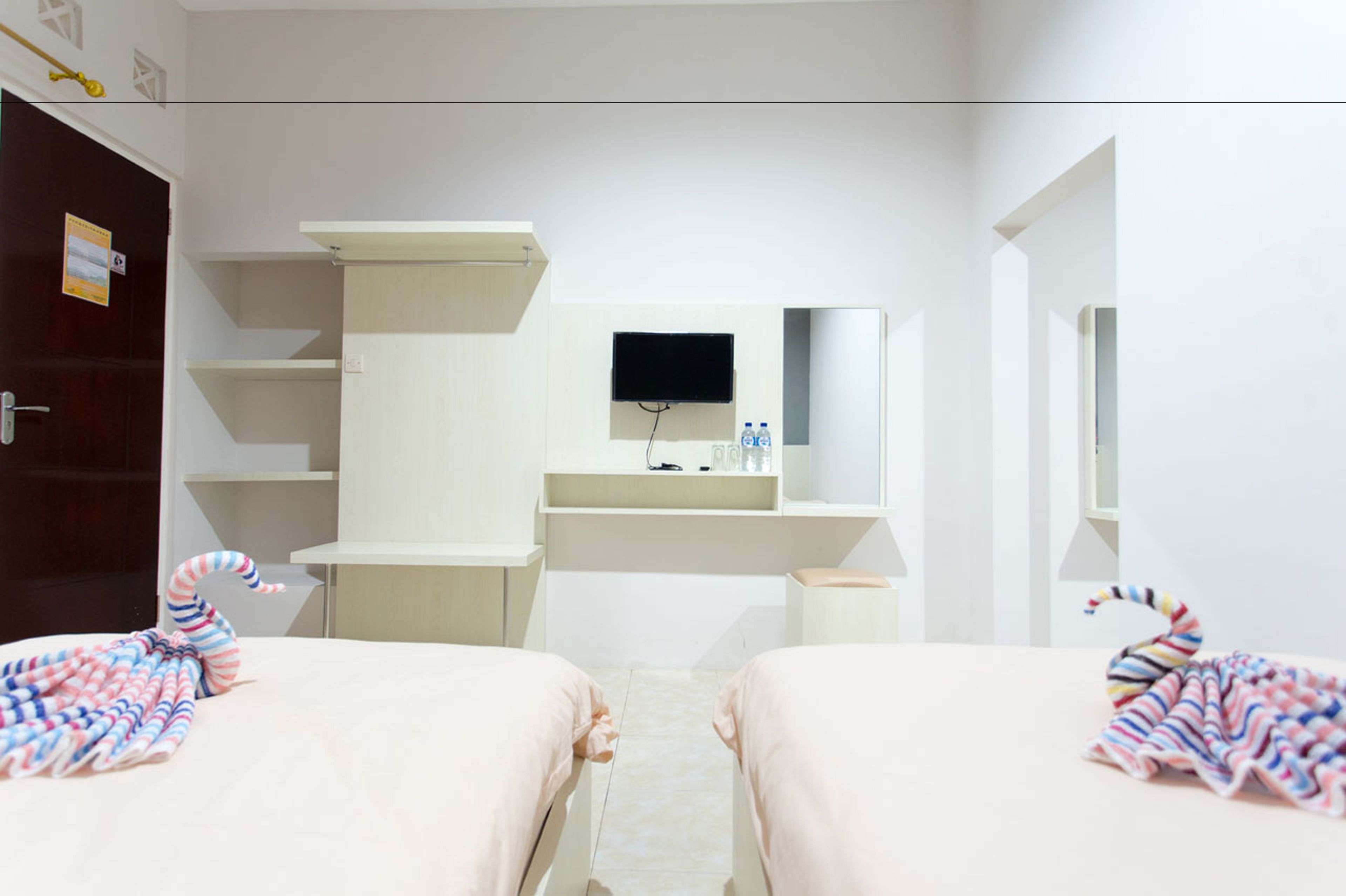A hotel room with two beds, a large mirror, a TV, and a minibar.