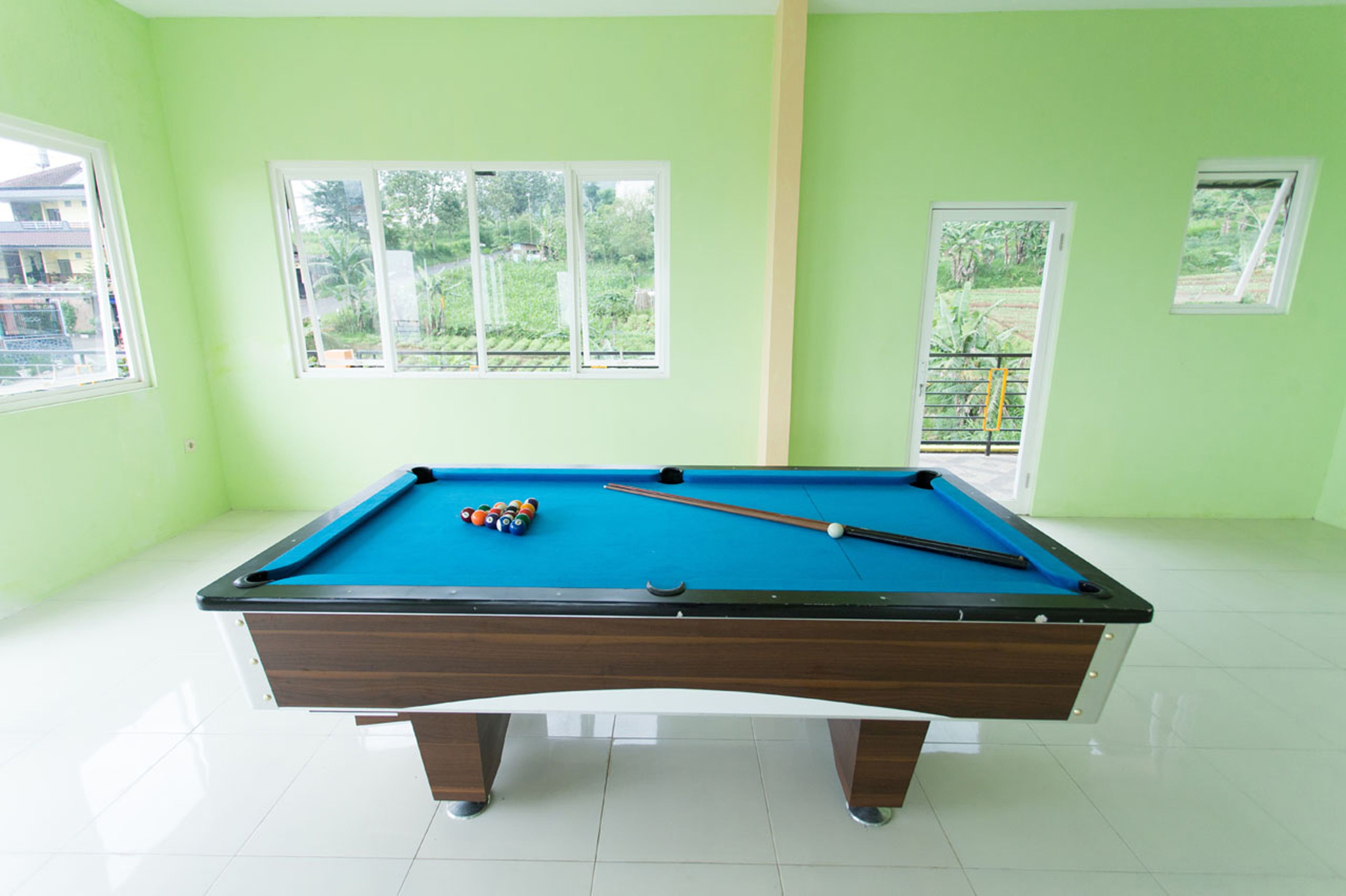 A pool table in a room with light green walls and white tiled flooring.