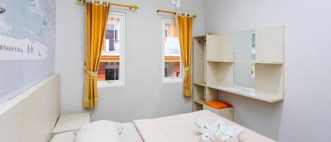 Una habitación de hotel con cama, ventana con cortinas, estante en la pared y una toalla sobre la cama.