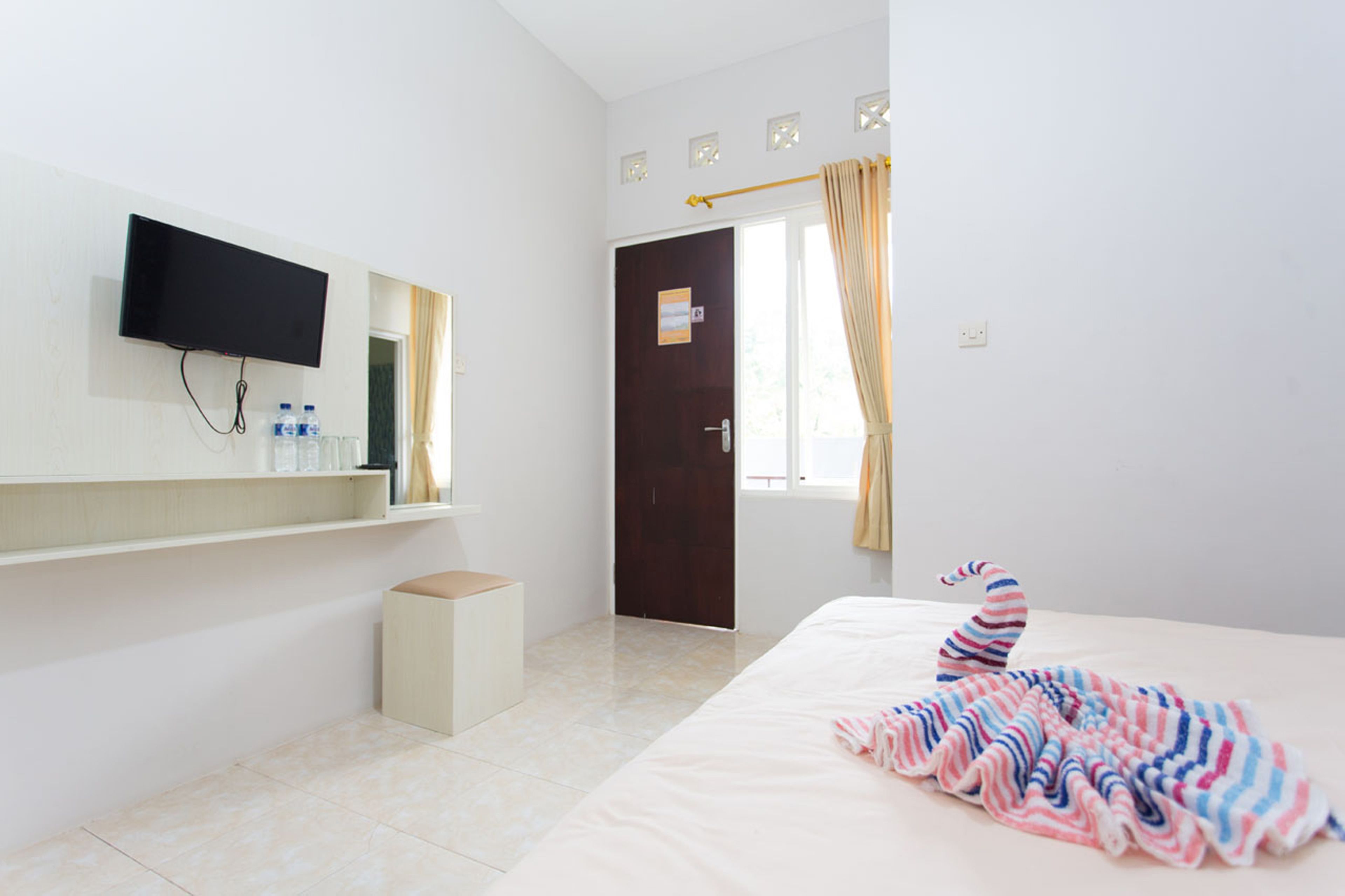 Una habitación de hotel con cama, televisor montado en la pared, una mesita y una puerta que da al exterior.