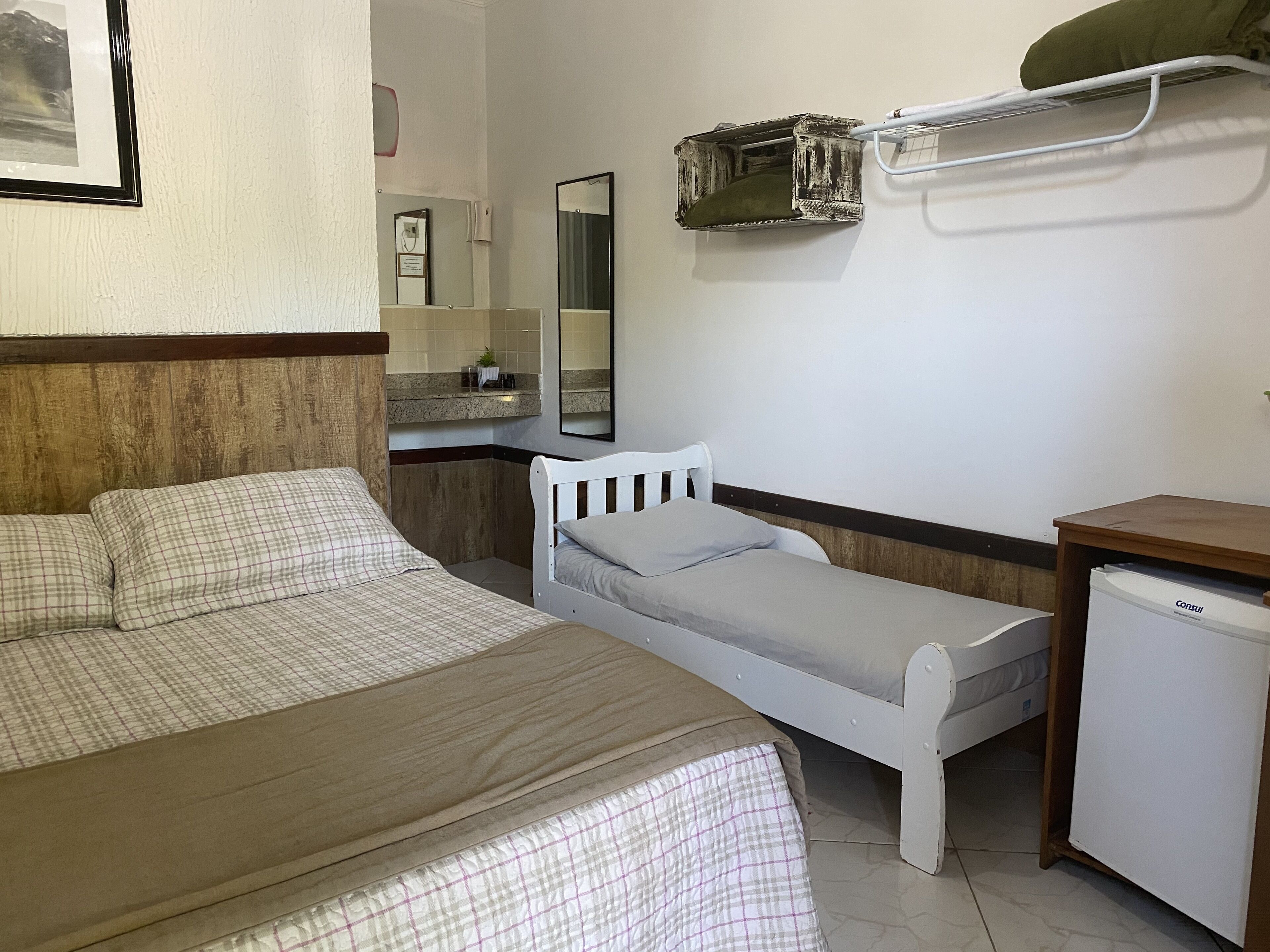 A hotel room with a large bed, a smaller bed, a desk, a mirror, and a refrigerator.