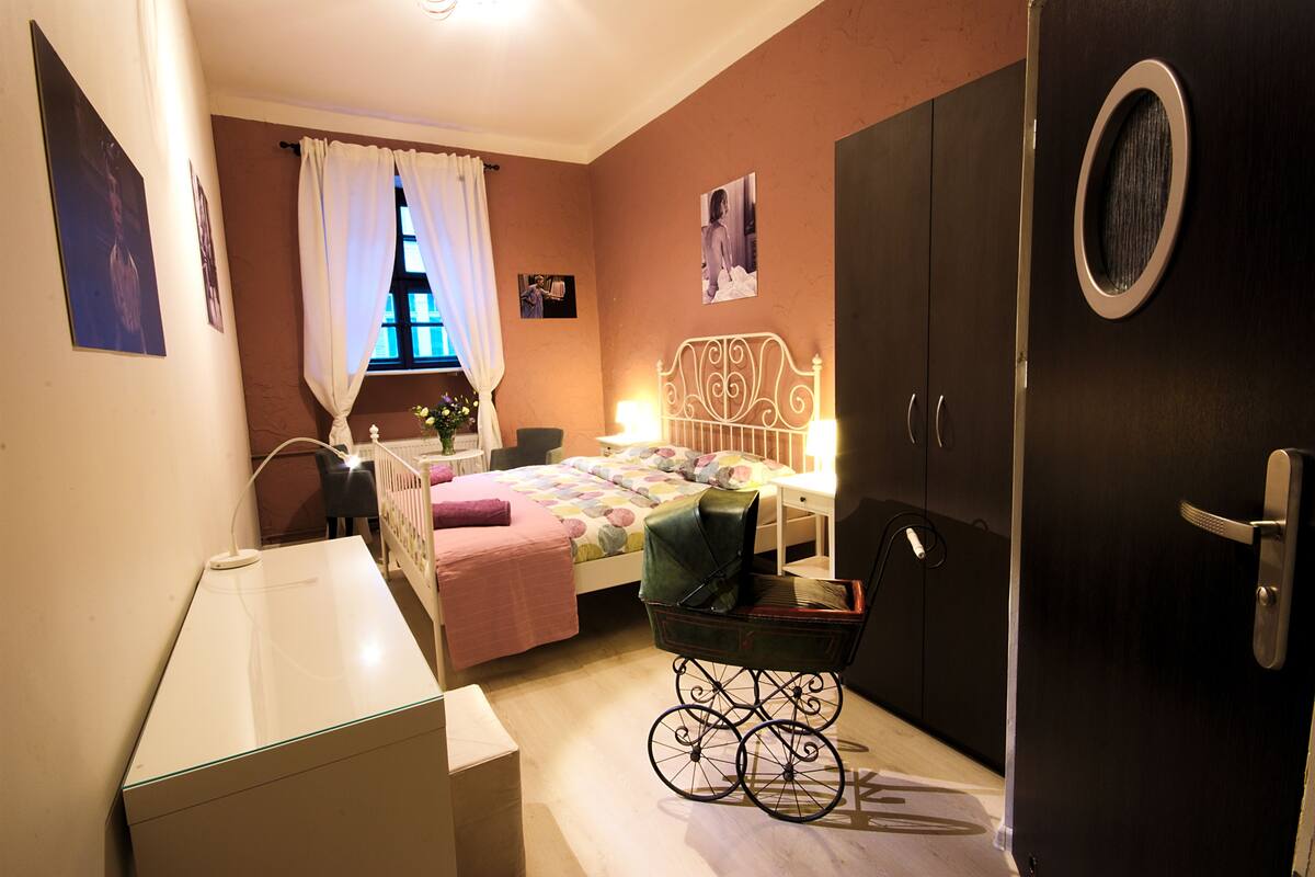 A bedroom with a bed, a crib, a desk, and a door.