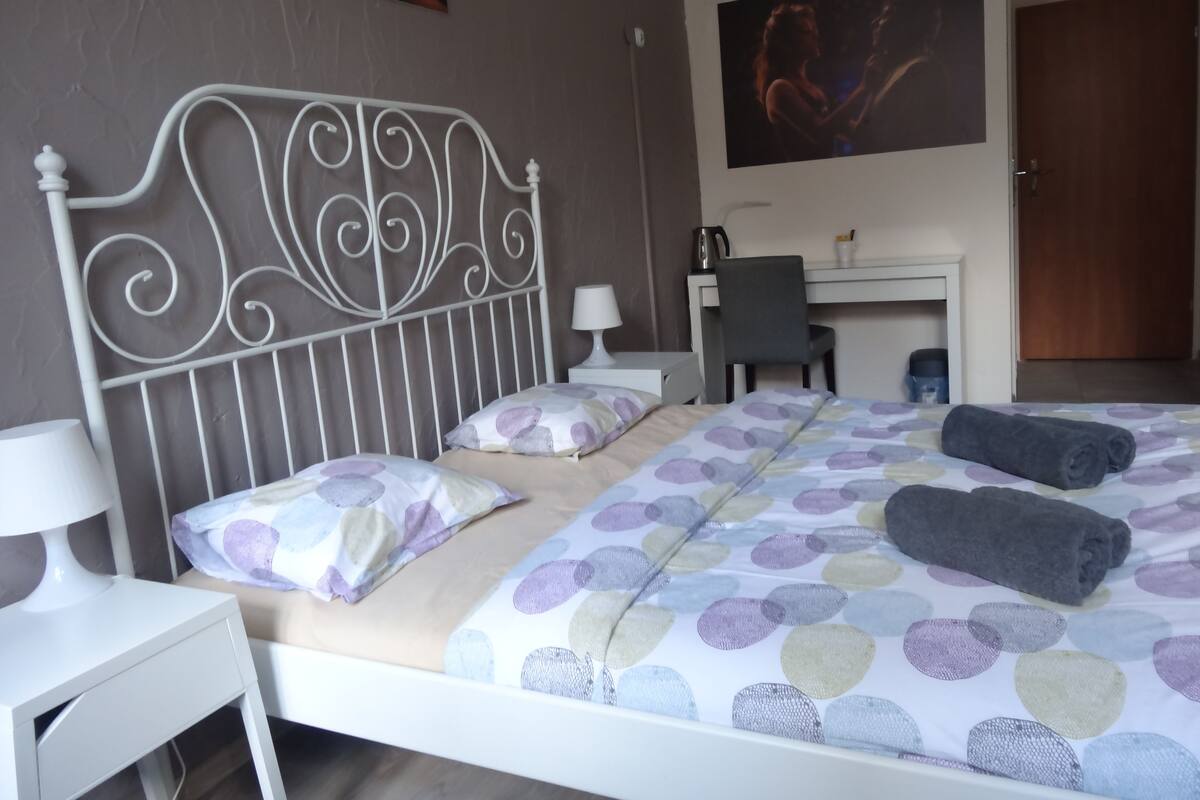 A neatly arranged bedroom with a bed, pillows, a desk, and a chair.