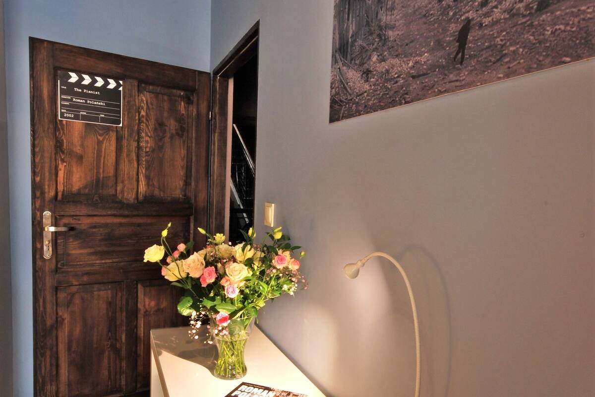 A reception area with a wooden door, a vase of flowers, a magazine on a glass table, and a wall-mounted lamp.